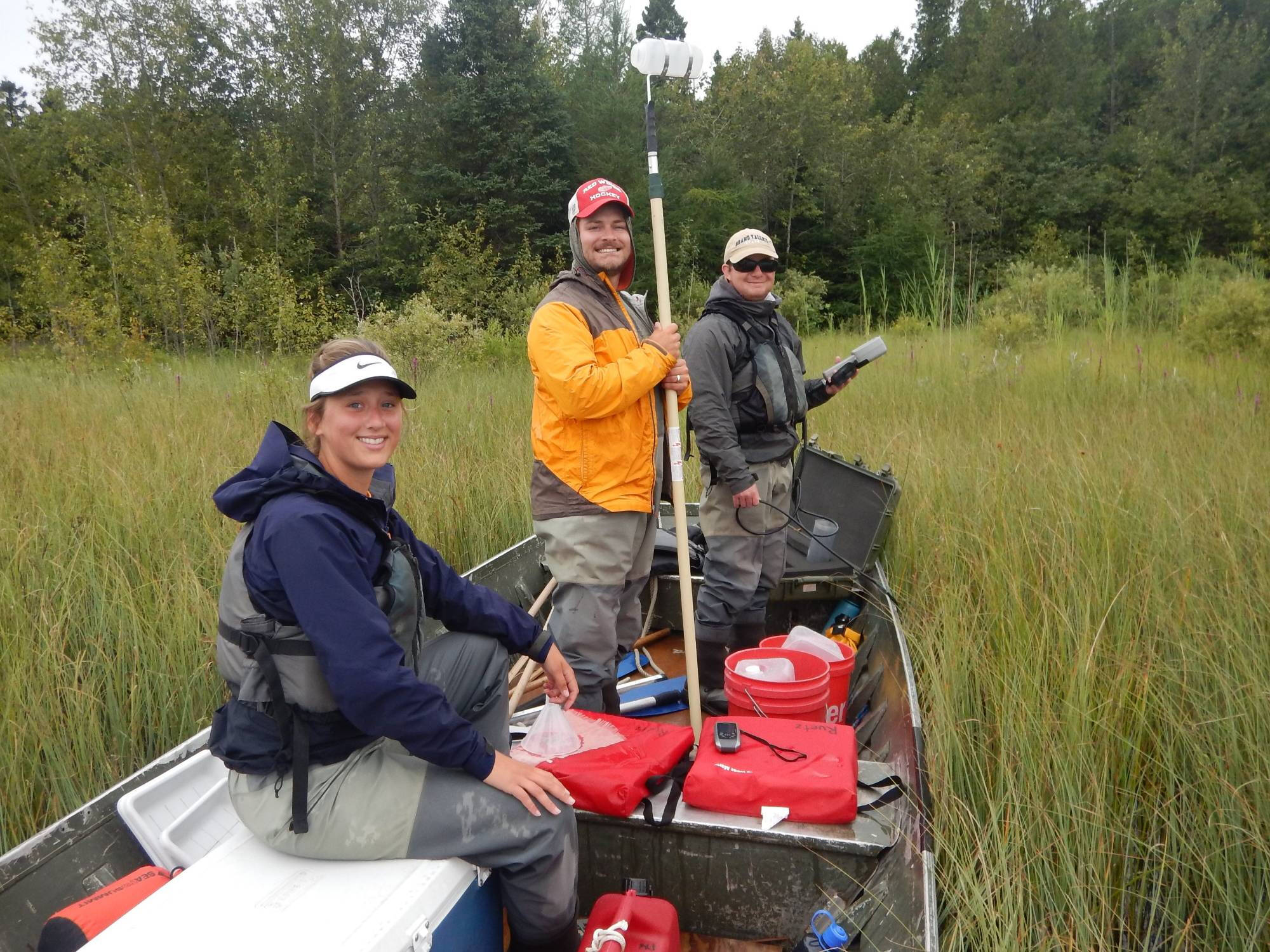 Three technicians pose for a photo in the jonboat among emergent vegetation.